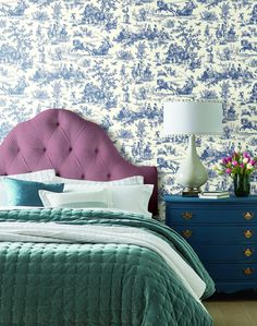 a bedroom with blue and white wallpaper has a purple upholstered headboard