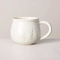 a white mug with trees on it sitting on top of a table next to a wall