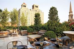 an outdoor dining area with tables and chairs in the foreground, surrounded by tall buildings