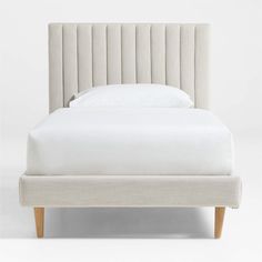 an upholstered bed with white sheets and pillows