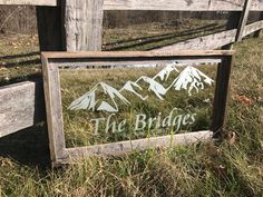 a wooden sign that says the bridges in front of some grass and trees with mountains behind it