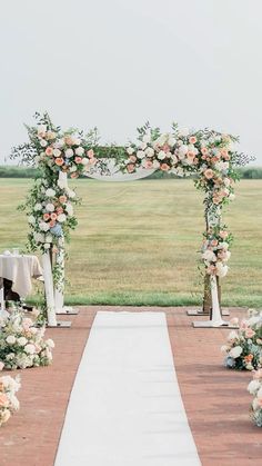 an outdoor ceremony setup with white and peach flowers on the aisle, along with greenery