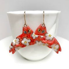 "Statement red cat earrings with white and gold floral patterns! The earring charms are handmade with porcelain clay. They are fired 3 times with underglaze colors, a mid-fire clear glaze, and a gold overglaze.  Average length of the charms is around 1 3/4\"\" and they are attached to gold-filled ear wires, 21 gauge. Care Instructions While porcelain clay is durable, it is not shatter-proof. Please wear and handle with care!  Earrings may be washed with soap and water if needed. Materials Porcel Whimsical Red Hand Painted Jewelry, Clay Underglaze, Cat Charm Necklace, Earring Hole, Porcelain Earrings, Earring Charms, Red Cat, Ceramic Pendant, Porcelain Clay