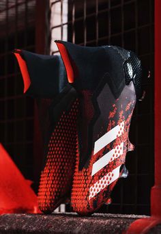 a pair of red and black soccer shoes sitting on top of a metal grate