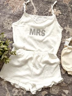 The Mrs. Pajama Satin PJ Set is the perfect gift for any bride-to-be, making it a delightful addition to a bridal shower celebration. This charming set features a personalized touch with sparkle letter patches, adding a unique flair that every bride will adore. Made from luxurious Swiss dot fabric, the set includes a matching cami tank and ruffle shorts, ensuring both comfort and style. The soft satin finish feels exquisite against the skin, making it ideal for cozy nights in or lounging with friends. The playful yet elegant design reflects the excitement of the upcoming wedding while providing a chic sleepwear option. It's a thoughtful present that combines practicality with a touch of glam, sure to make the bride feel special. Gift her this adorable PJ set, and she'll cherish the memorie Chic Sleepwear, Swiss Dot Fabric, Top And Bottom Set, Satin Pj Set, Letter Patches, Adult Pajamas, Dot Fabric, Bride Gift, Ruffle Shorts