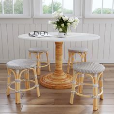 a white table with four stools and a vase on it in front of a window