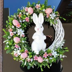 a white bunny sitting in front of a wreath with pink and white flowers on it