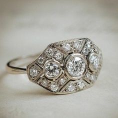 an antique diamond ring is shown on a white tablecloth, with the center stone surrounded by smaller round diamonds