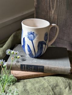 a blue and white coffee cup sitting on top of a book next to some flowers