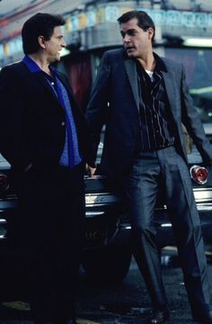 two men standing next to each other in front of a car