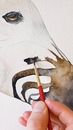 a person is holding a paintbrush and painting a horse's face on paper