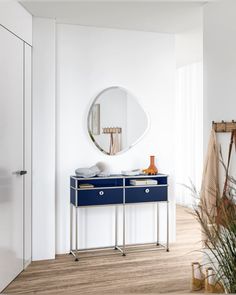 a white room with a blue dresser and mirror on the wall next to a potted plant