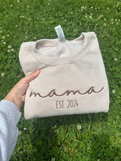 someone is holding up a sweater that says mama est 2024 on it in the grass