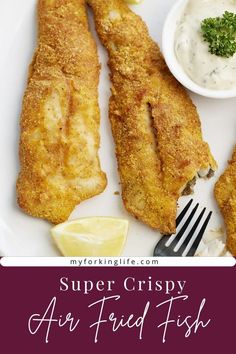 two fish sticks on a white plate with a fork and small bowl of sauce next to it