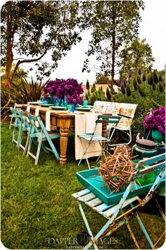 an outdoor table and chairs with purple flowers in the center, blue vases on each side