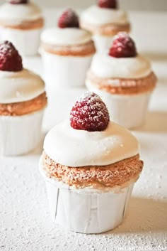 small cupcakes with white frosting and raspberries on top are lined up