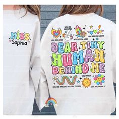 "Dear Tiny Human Behind Me Shirt, Teacher Shirt, Custom Teacher Name, Kindergarten Teacher, Back To School Shirt, Teacher Appreciation Gift ↓ Click here to view our additional fashionable collections ↓ https://handcraftedbyhelenn.etsy.com Product Details: - 100% Cotton (fiber content may vary for different colors) - Medium fabric (5.3 oz/yd2 (180 g/m2)) - Classic fit - Tear away label - Runs true to size Care instructions: - Machine wash: warm (max 40C or 105F); - Non-chlorine: bleach as needed; - Tumble dry: Medium - Do not iron; Do not dry clean ● Please choose your preferred style, size, and color from the dropdown menu or leave us a message in the \"notes to seller\" section. ● We are committed to processing and shipping your items as quickly as possible, but please note that custom pr Cute Long Sleeve Shirt With Text Print, Fun Long Sleeve T-shirt With Name Print, Multicolor Long Sleeve Shirt With Letter Print, Cute Long Sleeve Tops With Funny Text, Teacher Back To School, Kindergarten Teacher, Teacher Name, Teacher Appreciation Gift, Kindergarten Teachers