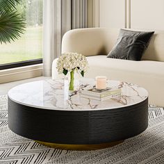 a marble coffee table with flowers on it in front of a couch and large window