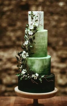 a three tiered green cake with white flowers on the top and bottom, sitting on a wooden table