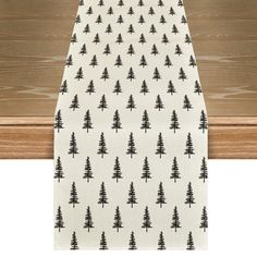 a white table runner with black pine trees printed on the front and bottom, hanging from a wooden frame