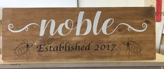 a wooden sign that says noble established in white lettering on it, with two hands holding the word noble