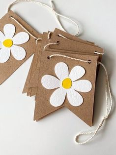 three brown paper tags with white and yellow flowers hanging from twine on the string