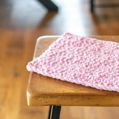 a pink crocheted dishcloth sitting on top of a wooden table next to a black chair