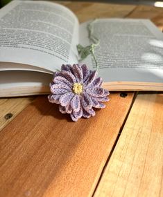 an open book sitting on top of a wooden table next to a purple and white flower