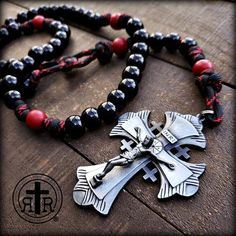 a black and red beaded necklace with an ornate cross on the front, sitting on top of a wooden table