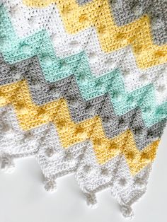 a crocheted blanket with yellow, grey and white squares on top of it