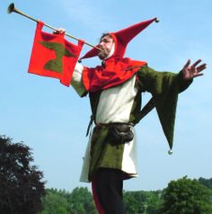 a man dressed in medieval clothing holding a flag and standing on top of a field