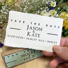 save the date card being held up by someone's hand with flowers in the background