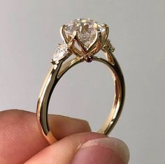 a person holding up a gold ring with two diamonds on it's sides and the middle