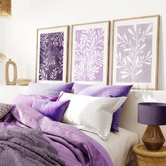 a bed with purple and white sheets in a bedroom next to two pictures on the wall