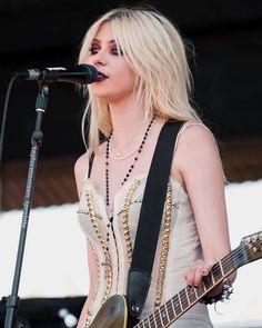 a woman with blonde hair is playing guitar and singing into a microphone at an outdoor concert