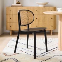 a black chair sitting on top of a rug next to a wooden table and dresser