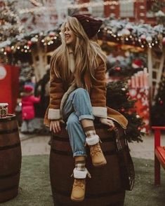 a woman sitting on top of a barrel next to a christmas tree