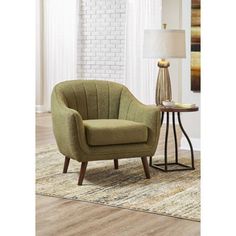 a green chair sitting on top of a wooden floor next to a table with a lamp