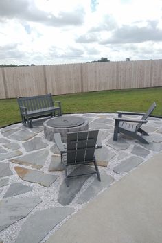 two wooden chairs sitting on top of a stone patio next to a fire pit in the middle of a yard