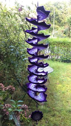 a tall purple sculpture sitting in the middle of a lush green field