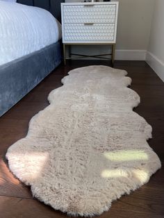 a white sheepskin rug on the floor next to a bed and night stand in a bedroom