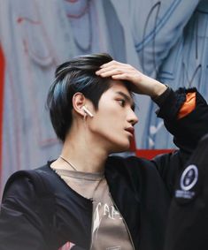 a man with black hair and ear piercings standing in front of graffiti covered wall