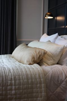 a bed with white sheets and pillows in a bedroom next to a lamp on the wall