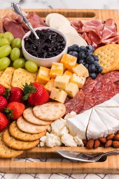 a wooden platter filled with cheese, crackers, fruit and meats on a table