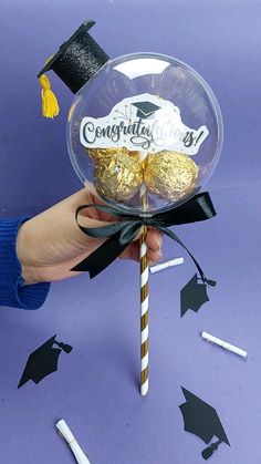 a hand holding a candy lollipop with graduation cap on it