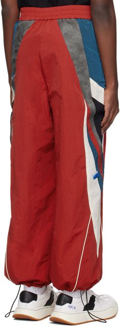 Nylon taffeta track pants. Piping and grained faux-leather trim throughout. · Paneled construction · Elasticized waistband · Two-pocket styling · Zip-fly · Logo embroidered at front · Bungee-style drawstring at cuffs · Full mesh lining Supplier color: Red Red Nylon Sporty Pants, Sporty Red Nylon Pants, Red Nylon Sports Pants, Ader Error, Red Panels, Fly Logo, Leather Trim, Logo Embroidered, Track Pants