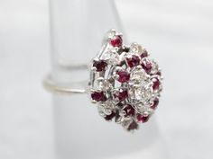 This sophisticated ring is crafted with lustrous white gold and adorned with shining white diamonds and sparkling red rubies. Each gem is carefully chosen and placed in a unified design, creating a stunning piece of jewelry to treasure for a lifetime.Metal: 14K White GoldGem: 11 Diamonds totaling .34 Carats, VS-SI in Clarity, H-I in ColorGem Measurements: 3.1 mm, RoundAccents: 16 Rubies totaling .64 CaratsRing Size: 5.75Marks: "14K-ODI" Stamped on the inside band Red Marquise Cut Diamond Ring, Formal Cluster Ruby Ring, Formal Ruby Ring With Diamond Accents In Cluster Shape, Diamond Cluster Ruby Ring With Diamond Accents, Ruby Ring With Diamond Cluster And Brilliant Cut, Cluster Ruby Ring With Brilliant Cut Diamonds, Ruby Cluster Diamond Ring, Cluster Ruby Ring With Diamonds, Formal Cluster Ruby Ring With Diamond Accents