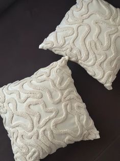 two white pillows sitting next to each other on a black surface with an embroidered design