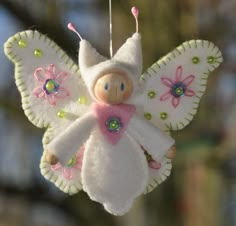 a white and pink doll hanging from a string with flowers on it's wings