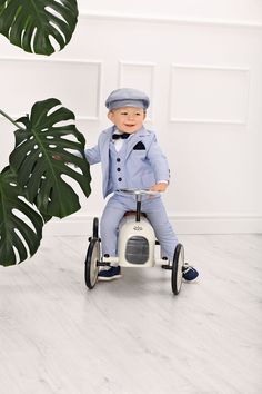 a little boy in a blue suit is riding a tricycle